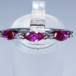 Pode incluir: Um anel de prata com três pedras preciosas de rubi em forma de marquesa e dois diamantes menores.