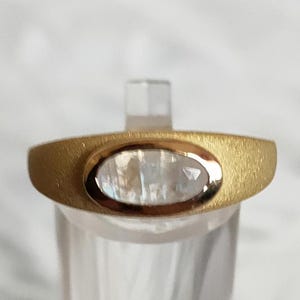 May include: A gold ring with a clear oval-shaped gemstone set in the centre.