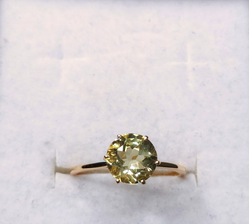 May include: A gold ring with a large, round, light green gemstone set in a prong setting.