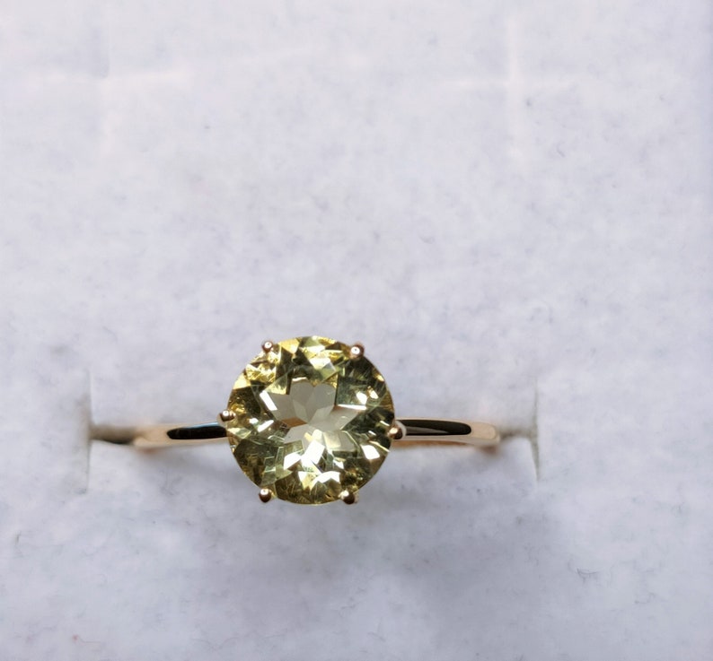 May include: A gold ring with a large, round, light green gemstone set in a prong setting.