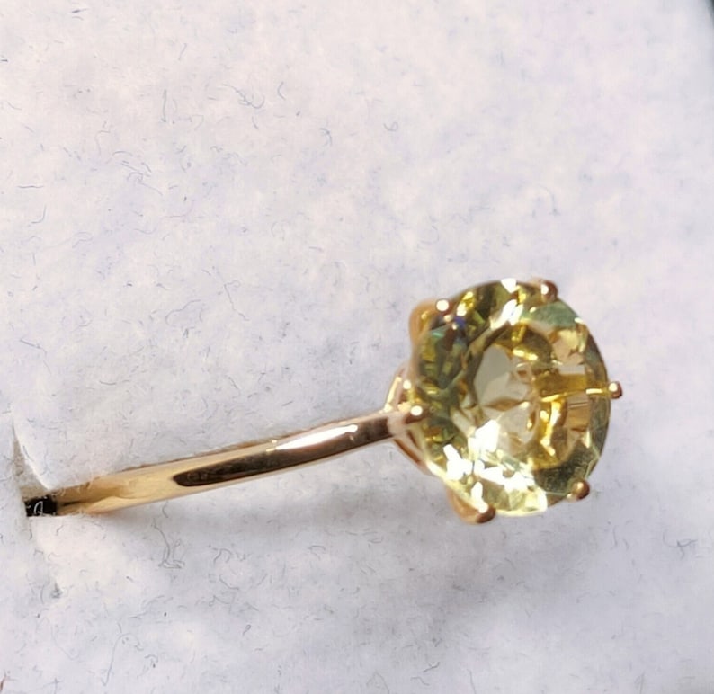 May include: A gold ring with a large, round, yellow gemstone set in a prong setting.