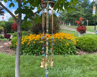 May include: A gold wind chime with multiple strands of colorful beads and bells hanging from a circular top. The chime is hanging from a tree branch in a garden setting.