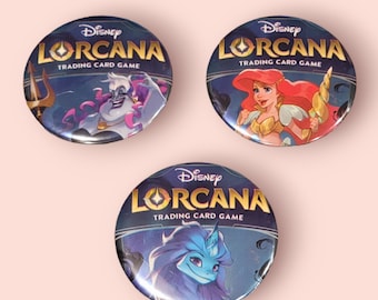 Può includere: Tre bottoni rotondi e colorati con il logo del gioco di carte collezionabili Disney Lorcana. I bottoni presentano diversi personaggi del gioco, tra cui Ursula, Ariel e una creatura blu simile a un unicorno.