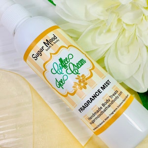 May include: White fragrance mist bottle with a label that reads "Coffee Ice Cream." The label has a yellow and white striped background with green and gold text. The bottle is surrounded by a white flower and yellow ribbon.