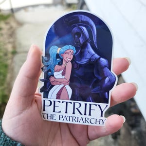 May include: A sticker featuring a cartoon illustration of a woman with blue hair and a warrior figure. The sticker has the text "PETRIFY THE PATRIARCHY" in white letters. The background is a dark blue with stars.