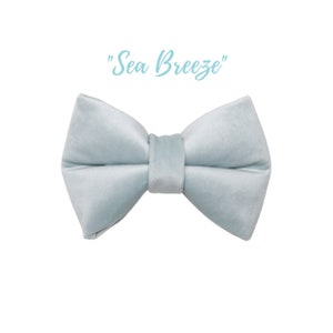 May include: A light blue bow tie made of satin fabric. The bow tie is tied and ready to wear. The text "Sea Breeze" is written above the bow tie.