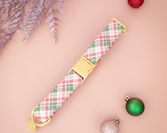 Op de afbeelding: Een hondenriem met een rood, groen en wit geruit patroon, met goudkleurige hardware. De afbeelding bevat kerstballen en zilveren decoratieve takjes op een roze achtergrond.
