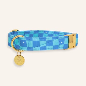 Super Trouper handmade dog collar in a bold blue plaid print with gold buckle and D-ring, photographed on a light neutral background.