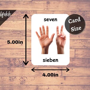 K&ouml;nnte beinhalten: Eine wei&szlig;e Karte mit dem Wort "seven" in schwarzer Schrift oben. Zwei H&auml;nde sind abgebildet, eine mit allen f&uuml;nf Fingern ausgestreckt und die andere mit zwei Fingern ausgestreckt. Das Wort "sieben" steht in schwarzer Schrift unten auf der Karte. Die Karte ist 12,7 cm hoch und 10,2 cm breit.