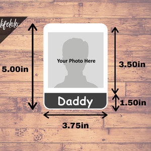 May include: A white photo frame with a black border and the word "Daddy" printed on the bottom. The frame is 3.75 inches wide and 5 inches tall. There is a placeholder for a photo in the center of the frame.