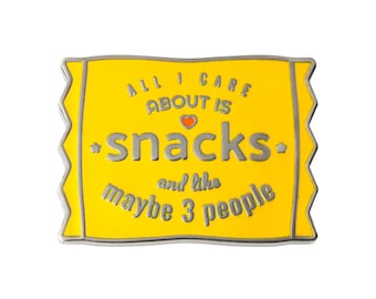 May include: Yellow enamel pin with a silver border. The pin is shaped like a snack bag and says "All I care about is snacks. And like maybe 3 people."