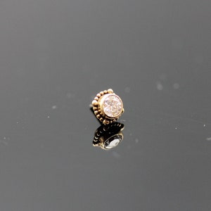 May include: A gold nose ring with a clear round gemstone.