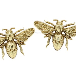 May include: A pair of gold bee earrings with intricate details. The bees are facing forward with their wings spread out.
