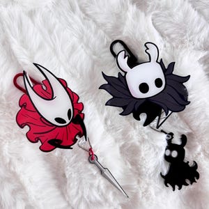 May include: Two character keyrings. One keyring features a red and white character with a silver sword. The other keyring features a black and white character with a small black character attached.