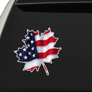 May include: A white car's rear window features a sticker. The sticker is a maple leaf design, with the left side displaying the American flag's stars and the right side showing the stripes. The leaf has a white border.