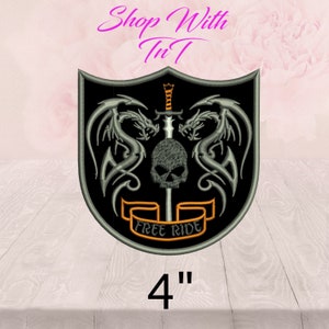 May include: Embroidered patch featuring a black shield design with two silver dragons flanking a skull and sword. The patch includes the text "FREE RIDE" on a banner and is 4 inches in size. The text "Shop With TnT" is at the top.
