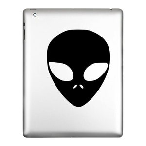 May include: A silver tablet with a black alien head graphic. The alien head is a simple, stylized design with large oval eyes and small nostrils. The tablet has a sleek, modern design.
