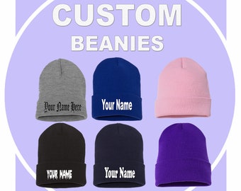 May include: Six custom beanies in different colours, including grey, blue, pink, black, navy, and purple. Each beanie has different text embroidered on it, including "Your Name Here", "Your Name", and "YOUR NAME".