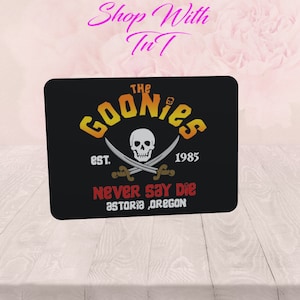 Può includere: Tappetino per mouse nero con una grafica gialla, arancione e rossa di un teschio e ossa incrociate con il testo "The Goonies Est. 1985 Never Say Die Astoria, Oregon"