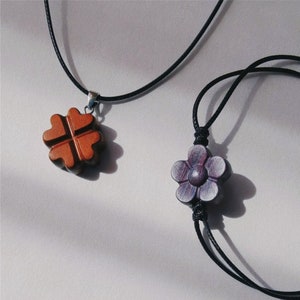 May include: Two necklaces with wooden pendants. One necklace has a four-leaf clover pendant in brown. The other necklace has a flower pendant in purple.