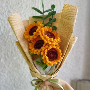Op de afbeelding: Een boeket van vier gele en bruine viltzonnebloemen verpakt in bruin papier met een groen lint.