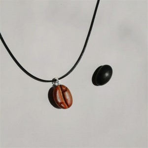 May include: A black cord necklace with a wooden coffee bean pendant. The pendant is brown and has a detailed carving.