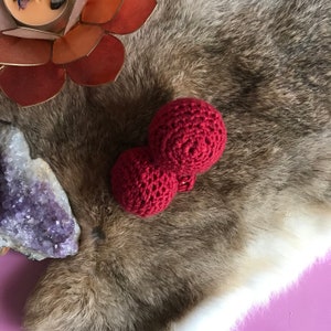 Puede incluir: Un lazo de crochet rojo con dos bucles. El lazo está sobre una superficie peluda marrón y blanca.