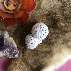 May include: Two white crocheted balls on a brown faux fur surface. The balls are round and have a textured surface.