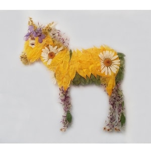 May include: A yellow horse created from pressed flowers and leaves. The horse has a purple flower crown and white daisy accents.