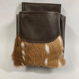 May include: A brown leather pouch with a brown and white fur flap. The pouch has a zipper closure and a small pocket on the front.