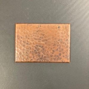 May include: A small, square, hammered copper tile with a textured surface.
