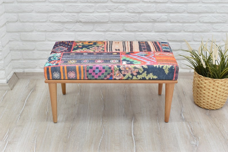 Pode incluir: Banqueta retangular com um tampo com padr&atilde;o de retalhos em v&aacute;rias cores, incluindo laranja, azul e rosa. A banqueta tem pernas de madeira castanho-claro e uma estrutura de madeira castanho-claro. A banqueta tem aproximadamente 100 cm de comprimento.