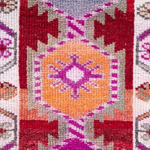 May include: A close-up of a colorful woven rug with a geometric pattern. The rug features shades of red, orange, pink, and white.