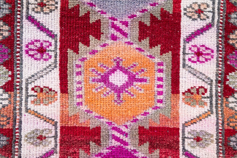 May include: A close-up of a colorful woven rug with a geometric pattern. The rug features shades of red, orange, pink, and white.