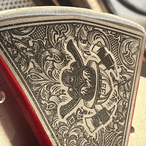 May include: Close-up of a silver axe head with an intricate engraved design. The design features a firefighter's helmet with flames and an axe. The axe head is attached to a red handle.