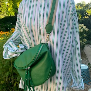 May include: A green leather crossbody bag with a zipper closure and a long strap. The bag is worn over a white and green striped shirt.