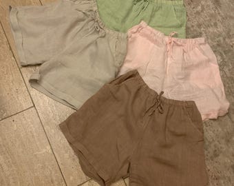 Pode incluir: Uma coleção de quatro pares de calções com cintura elástica e cordão de ajuste. Os calções estão disponíveis em verde claro, bege, rosa claro e castanho, cada um desenhado com um corte descontraído e bainhas dobradas nas pernas.