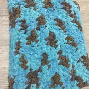 Könnte beinhalten: Eine weiche, plüschige Decke in Blau- und Brauntönen. Die Decke hat ein sich wiederholendes Muster aus braunen Formen auf blauem Hintergrund. Die Textur scheint aus dickem, geschlungenem Garn zu bestehen.