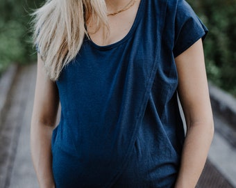 May include: A woman wearing a dark blue, short-sleeved, wrap-style top. The top has a scoop neckline and a gold chain necklace.