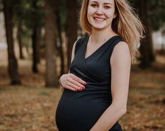 May include: A pregnant woman wearing a black sleeveless top, smiling and holding her belly in a forest setting.