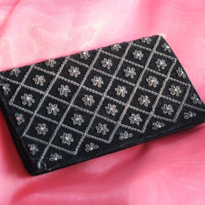 May include: A black velvet clutch purse with a silver floral pattern. The purse is closed and lying on a pink fabric surface.