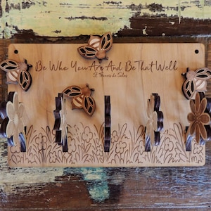 May include: Wooden key holder with a bee and flower design. It has the quote "Be who you are and be that well, St. Francis de Sales" engraved on it.
