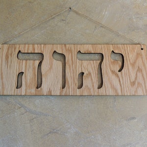 The sign is shown hanging from twine on a beige wall.