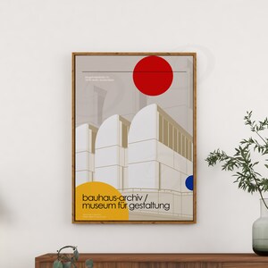 May include: A minimalist poster with a geometric design of a building in white, beige, and gray. The poster has a red circle at the top and a blue circle at the bottom. The text "bauhaus-archiv/museum f&uuml;r gestaltung" is in yellow at the bottom of the poster.