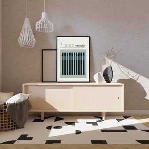 May include: A light beige cabinet with a sliding door, a black and white geometric rug, and a black framed poster with the word "Interstellar" on it. Two white pendant lights hang from the ceiling.