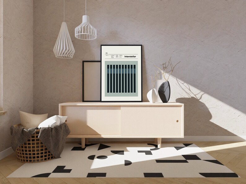 May include: A light beige cabinet with a sliding door, a black and white geometric rug, and a black framed poster with the word "Interstellar" on it. Two white pendant lights hang from the ceiling.