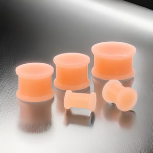 May include: A set of five flesh-colored silicone ear gauges in various sizes. The gauges are smooth and have a slightly rounded shape.