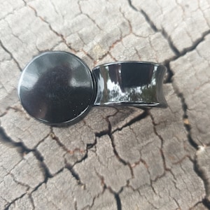 May include: Two black ear gauges, one round and one flared, made of polished acrylic.