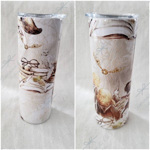 May include: A white stainless steel tumbler with a Harry Potter themed design. The design features a white owl, a golden snitch, and a stack of books. The tumbler is 20 ounces.