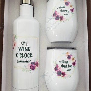 May include: A set of three white stainless steel tumblers with floral designs and wine-themed sayings. The tumblers include "It's Wine O'Clock Somewhere", "Smile There's Wine", and "Always Time for Wine".